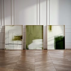 three abstract paintings are on the floor in front of a white wall and wooden floors