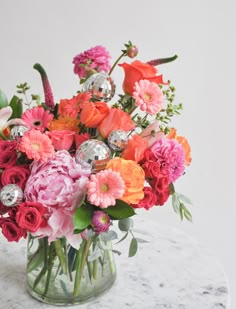 a vase filled with lots of colorful flowers on top of a marble table next to a white wall