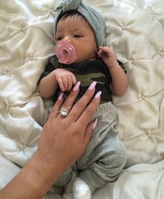 a woman holding a baby with a pacifier in it's mouth while laying on a bed