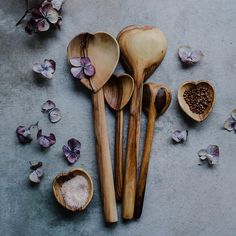 wooden spoons and bowls filled with sea salt on top of a gray surface next to dried flowers