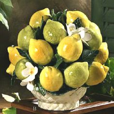 a vase filled with lots of lemons on top of a wooden table next to flowers