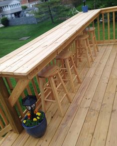 a wooden deck with barstools and flowers on the planter box next to it