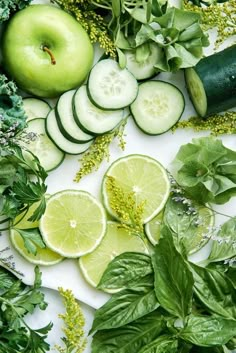 sliced cucumbers, leaves, and other vegetables are arranged on a white surface