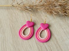 the pink and white earrings are hanging from gold earwires on a wooden surface