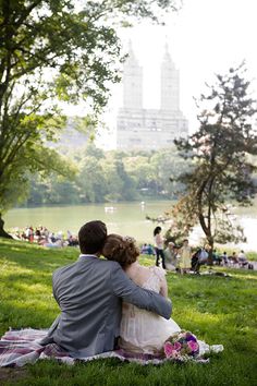 a man and woman sitting on top of a blanket next to each other in the grass