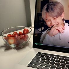 an open laptop computer sitting next to a bowl of strawberries