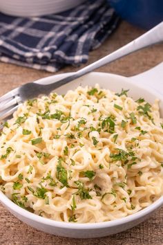 a white bowl filled with pasta and parsley on top of a table next to a fork