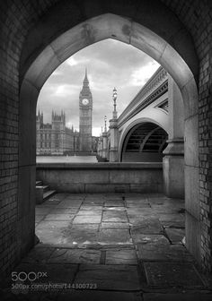 the big ben clock tower towering over the city of london from under an archway in black and white