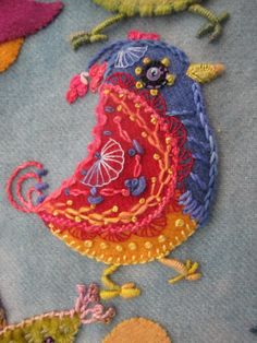 a close up of a bird on a blue surface with different colored threadwork designs