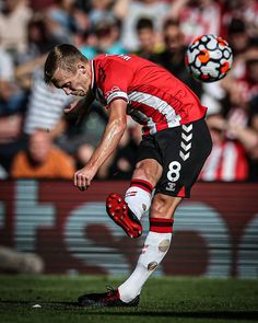 a man kicking a soccer ball on top of a field with people watching in the stands