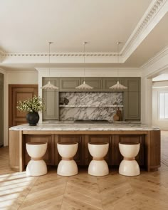 a kitchen with marble counter tops and white stools in front of an island that has four vases on it