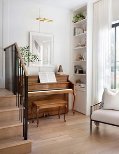 a living room filled with furniture and a piano in front of a window next to a stair case