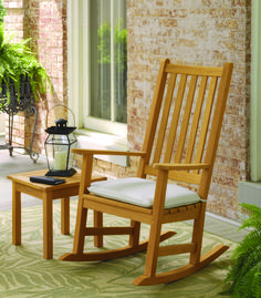 a wooden rocking chair sitting on top of a rug next to a table with a lamp