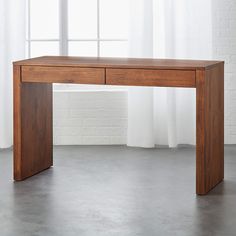 a wooden table with two drawers in front of a white brick wall and curtains behind it