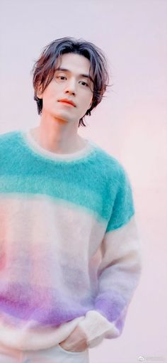 a young man with long hair wearing a multicolored sweater