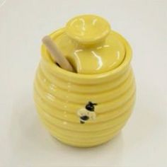 a yellow ceramic jar with a lid and spoon in the shape of a bee on it