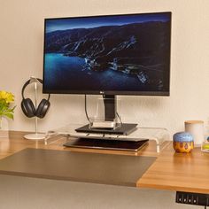 a flat screen tv sitting on top of a wooden desk next to a vase with flowers