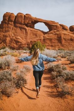 a woman is walking through the desert with her arms spread out in front of an arch