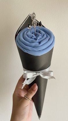 a hand holding a black and blue cupcake with silver ribbon around it's edges