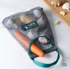 a mesh bag filled with carrots and garlic on top of a counter next to a cutting board