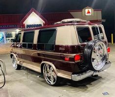 a maroon and tan van parked in front of a building at night with its lights on