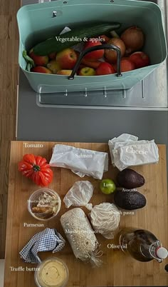 an assortment of fruits and vegetables are displayed on a cutting board next to a basket of apples