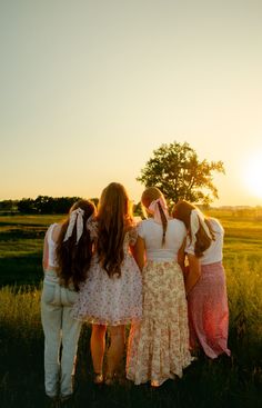 three girls are standing in the grass with their backs to each other as the sun sets