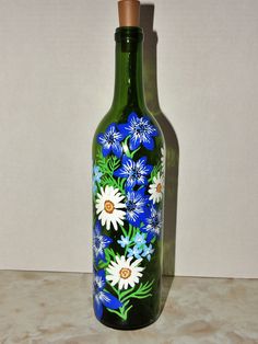 a green glass bottle with blue and white flowers painted on the bottom is sitting on a counter