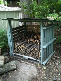 a pile of logs sitting inside of a wooden shed next to a tree filled forest