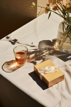 A serene scene showcasing a glass of tea and an unopened boxed tea gift amidst a luxe setting. Liminal Space, Tea Culture, Golden Light