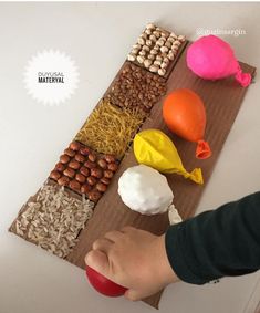 a child is playing with food on a wooden board that includes eggs, nuts and other things