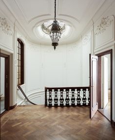 an empty room with wooden floors and white walls, chandelier above the door