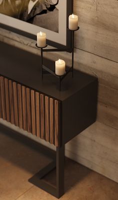 two candles are lit on a console table in front of a framed photograph and wood paneling