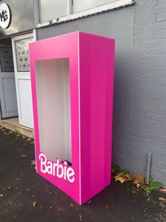 a pink box with the word barbie on it sitting in front of a gray building