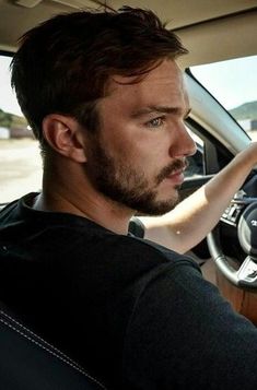 a man sitting in the driver's seat of a car with his hand on the steering wheel