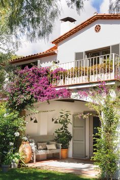 a white house with purple flowers on the balcony