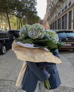 a woman is walking down the street with flowers in her hand and wearing a blue jacket