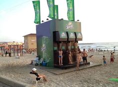 some people are standing on the beach near a water fountain