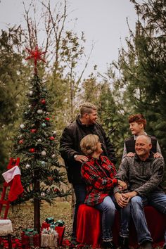 a family sitting on a bench in front of a christmas tree with presents around it