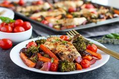 a white plate topped with chicken and veggies next to a pan of tomatoes