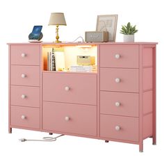 a pink dresser with many drawers and a lamp on top of it, in front of a white background