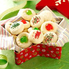 small christmas cookies in a red and white box on a green tablecloth next to other holiday decorations