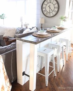 a living room with a couch, table and stools in front of a clock on the wall