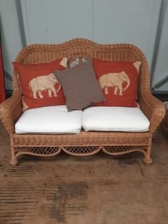 a wicker couch with two pillows on it and an elephant pillow in the back