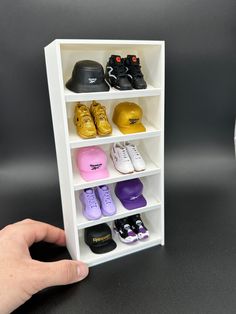 a hand is holding a toy shelf with shoes on it and other items in the background