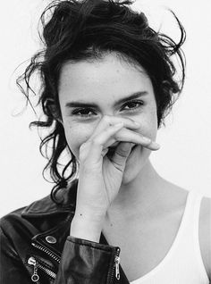 a black and white photo of a woman with her hand on her face while looking at the camera