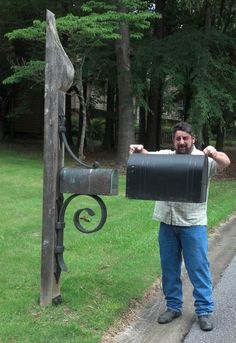 a man standing next to a mailbox on the side of a road in front of trees