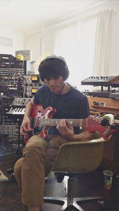 a man sitting in a chair playing an electric guitar with headphones on his ears