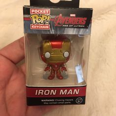 a small iron man toy in a box on a white surface with a hand holding it