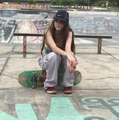 a young woman sitting on top of a skateboard in front of a graffiti covered park